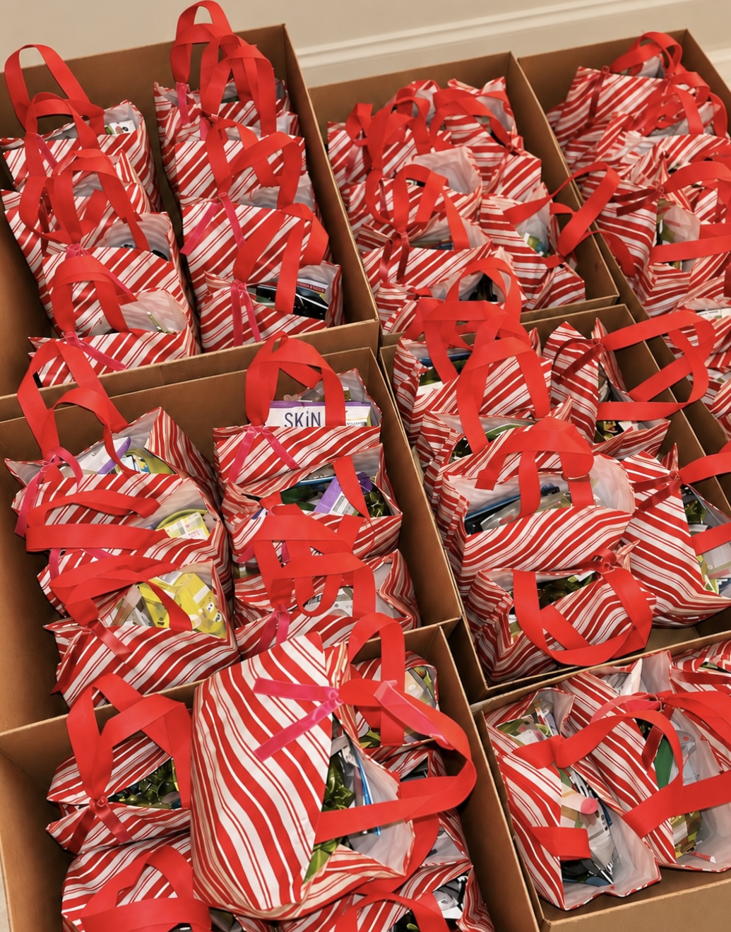 Red-and-white striped Christmas goodie bags with red handles, packed into cardboard boxes.